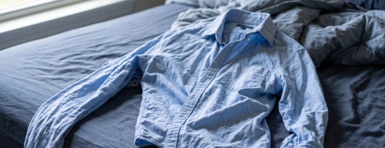 Camisa social azul-claro muito amassada jogada sobre uma cama desfeita.