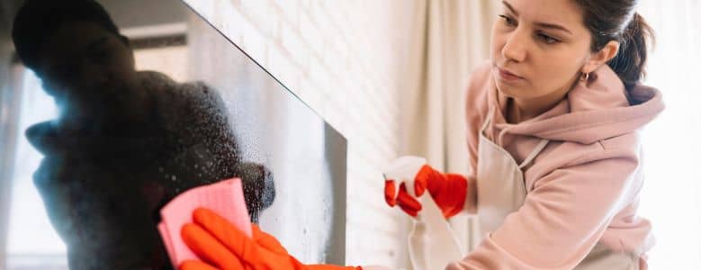 Mulher limpando eletrodoméstico com pano e produto de limpeza.
