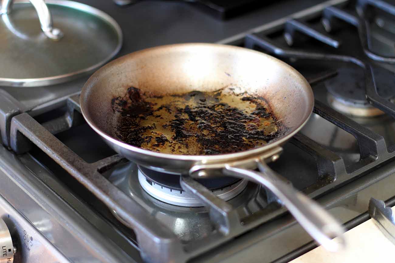Frigideira de alumínio, sobre um fogão, com a parte interna queimada